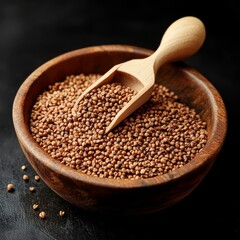 Brown buckwheat grains in wooden bowl and scoop on black.