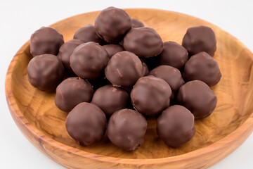 Obraz premium Chocolate covered nuts in wooden bowl. White chocolate ball with a white background. Chocolate balls lying on a wooden plate with white background. Chocolate balls lying on a lifestyle white plate.