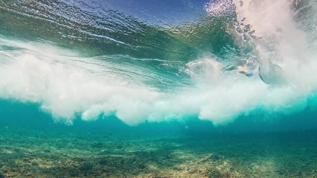 Teen boy surfer dives under the wave with surfing board
