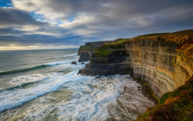 Ocean waves crashing against a rugged cliffside under a dramatic overcast sky
