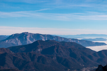 Majestic mountain peak Dobratsch seen from top of mount Piper in Julian Alps, Friuli Venezia Giulia, Italy. Lush green rolling hills with dense forest in Carinthia, Austria. Valley covered in clouds