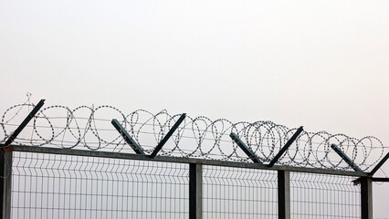 Security fence topped with barbed wire in a misty environment
