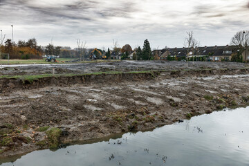 Construction site, muddy ground, and residential area in background.  Heavy earthmoving equipment...