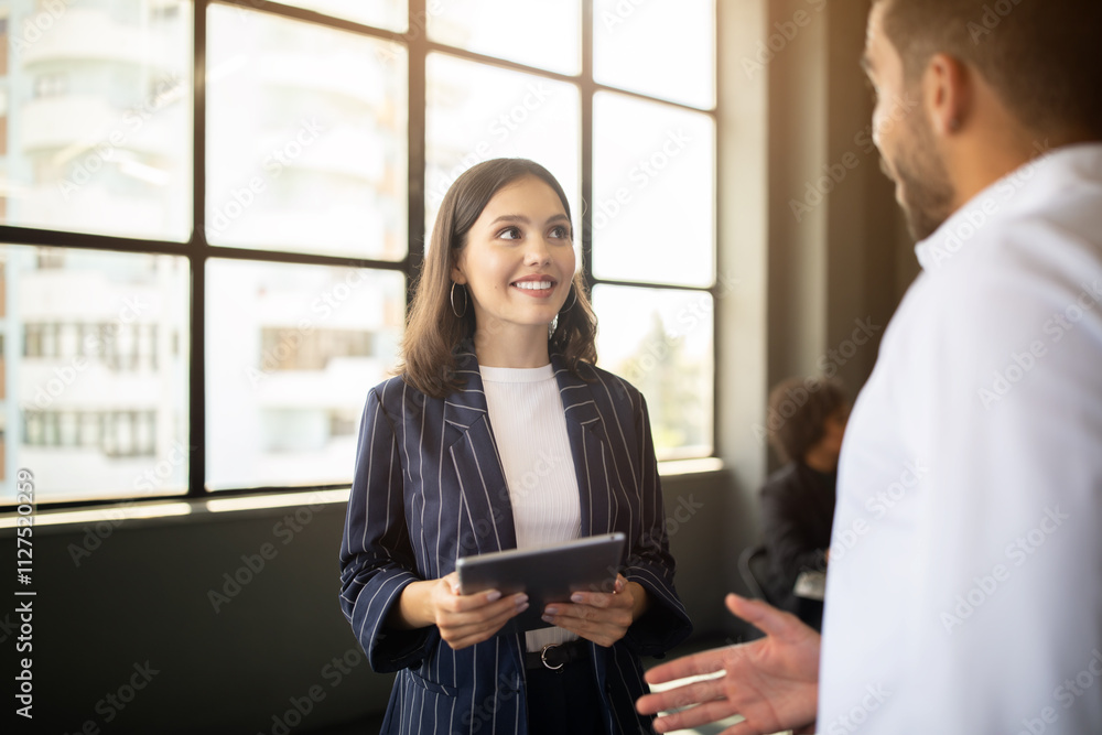 Poster two professionals are interacting in a bright office space. one person is holding a tablet, while th