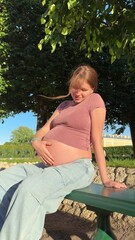 beautiful pregnant young woman walking in park in warm summer weather enjoying third trimester in...