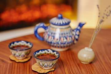 Hand-painted ceramic teapot and cups set on a wooden table, radiating warmth and tradition. Cozy atmosphere enhanced by dried lavender in a minimalist vase and soft ambient lighting