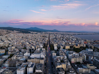 Aerial shot of Thessaloniki city center at sunset, with vibrant clouds above busy streets and tall buildings, overlooking the Thermaic Gulf in Greece