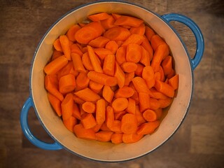 A top-down view of freshly cut carrots in a blue-handled pot on a wooden surface, ideal for cooking and healthy recipes.