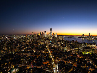 Stunning aerial view of New York City skyline at sunset with one world trade center in the Financial District of Lower Manhattan, illuminated buildings, and East River