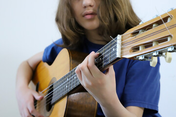 Long-haired teenage boy playing classical guitar. Student in music lessons. Stringed instrument. Background with copy space.
