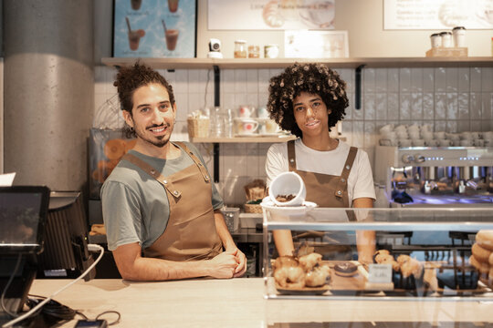 Friendly cafe workers behind counter with baked goods display