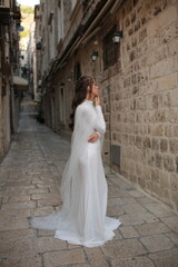 Obraz premium beautiful bride dressed in a white dress stands in the middle of the old town. wedding photoshoot in the old town of Croatia. old medieval castle