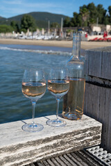 Bottle and glass of cold rose wine from Provence and wooden yacht boota pier on white sandy beach Plage de Pampelonne near Saint-Tropez, summer vacation in France