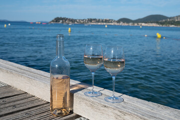 Tasting of cold rose wine from Provence outdoor on wooden yacht pier with view on blue water and white sandy beach Plage de Pampelonne near Saint-Tropez, summer vacation in France