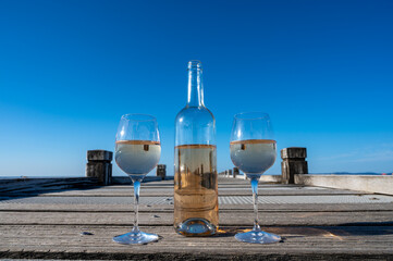 Tasting of cold rose wine from Provence outdoor on wooden yacht pier with view on blue water and white sandy beach Plage de Pampelonne near Saint-Tropez, summer vacation in France