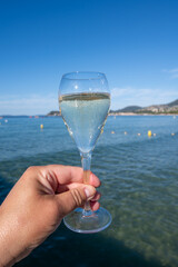 Summer time in Provence, hand with glass of cold champagne cremant sparkling wine on famous Pampelonne sandy beach near Saint-Tropez in sunny day, Var department, France, beach club party