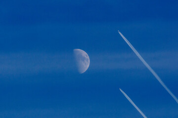 A crescent moon and two jet contrails are visible against a clear, deep blue sky.