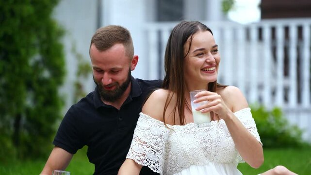 Happy cheerful Caucasian couple drinks milk. People having rest at the picnic outdoors. Blurred backdrop.