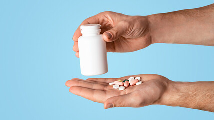 Unrecognizable young guy holding bottle of meds and different pills on light background, space for design. Panorama