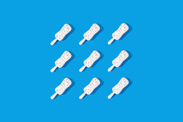 Pattern of white chocolate ice cream on a stick on a blue background. Minimal food photo concept, top view