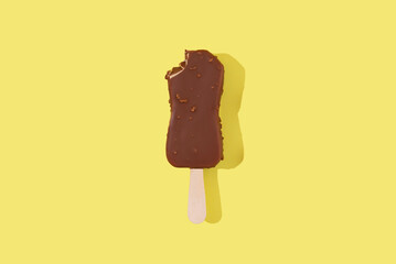 Сhocolate ice cream on a stick with nuts and chocolate glaze on a yellow background. Minimal food photo concept, top view