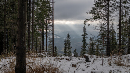 Sun rays from clouds on hilly landscape with snow.
