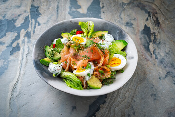 Traditional German mixed salad with graved salmon glavlax, eggs and avocado served as close-up in a Nordic design bowl