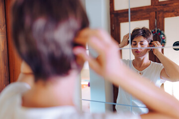 A woman with cancer is seen adjusting her wig in front of a mirror, capturing a moment of self-care...