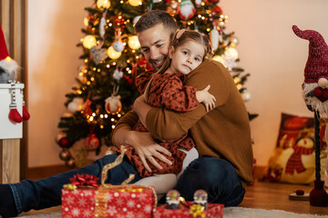 Portrait of loving farther hugging his little girl near christmas tree at home on christmas.