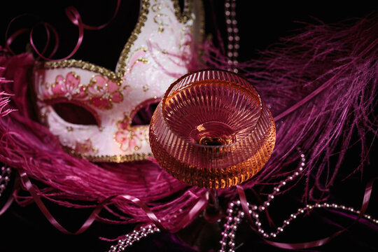 Masquerade ball holiday background. Glass of rose champagne, Venetian carnival mask and feathers on dark burgundy velour background - Powered by Adobe