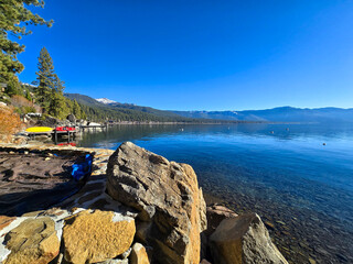 a gorgeous winter landscape at Lake Tahoe with blue lake water, lush green trees and plants and...