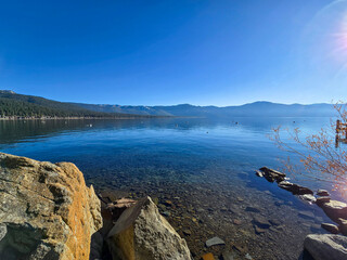 a gorgeous winter landscape at Lake Tahoe with blue lake water, lush green trees and plants and...