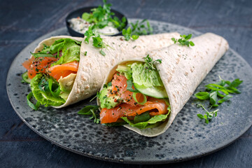 Italian style wrap piada tortilla with cured graved salmon, salad and avocado served as close-up with sour cream dressing dip on a Nordic Design plate