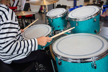 Child Playing Turquoise Drum Set: Hands Holding Drumsticks in a Music Classroom
