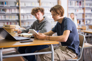 Two teenage friends are reading books and preparing for exams in the school library