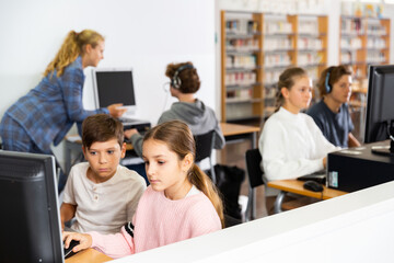 Group of young girls and boys sitting in computer classroom of library and exercising.