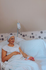 A smiling woman with cancer rests comfortably on a hospital bed, showcasing a moment of positivity...