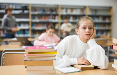 Fototapeta premium Bored teenage girl trying to prepare for exam in school library