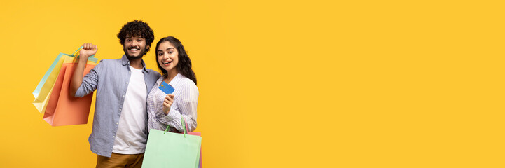 Easy payment. Portrait of indian couple showing debit credit card holding shopper bags after...