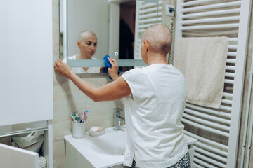 Obraz premium A dedicated woman suffering from cancer is focused on cleaning her bathroom mirror, emphasizing her attention to detail and the importance of cleanliness in her life.