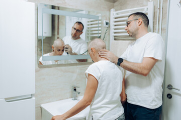 Obraz premium A caring individual is attentively shaving the head of another in a modern bathroom setting, showcasing the profound connection and emotional support shared between them in this intimate moment.