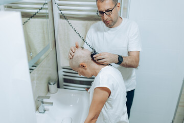 Obraz premium Woman with cancer support. A close interaction is seen as one individual shaves another's head, set in a bright bathroom that enhances the focus on personal grooming and care.