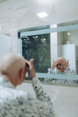 A person is seen in a bathroom mirror, thoughtfully applying makeup, symbolizing introspection and...