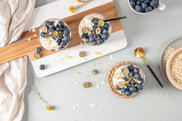 Three healthy blueberry Lemon Overnight Oats topped with blueberries, lemon zest and coconut shavings on a light blue wooden counter. Top view