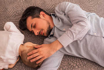 A young father shares love with his son and spends time together at home, lying on the bed, top view.