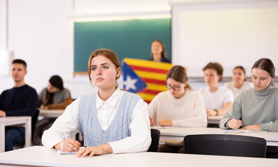 Students study in classroom, teacher stands behind with flag of Catalonia