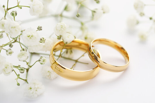 Golden wedding rings and flowers on white background, closeup