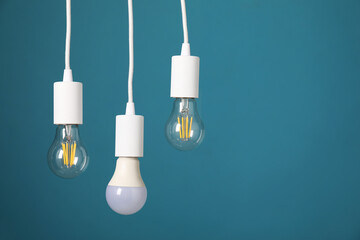 Light bulbs hanging on cords against light blue background, space for text