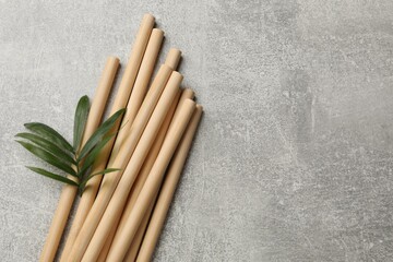 Bamboo drinking straws and green leaves on grey textured table, top view. Space for text