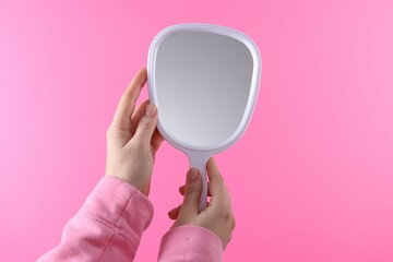 Woman holding handheld mirror on pink background, closeup